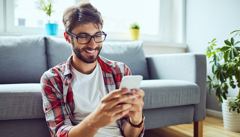 Rapaz segurando o celular, sorrindo e com aspecto otimista