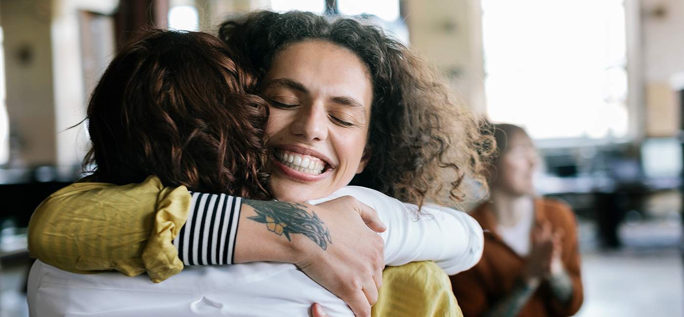 Duas mulheres se abraçando e sorrindo, represensando um ar de felicidade.