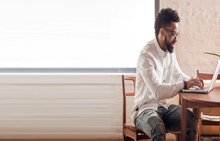 Homem negro sentado em frente ao computador, planejando sua vida financeira