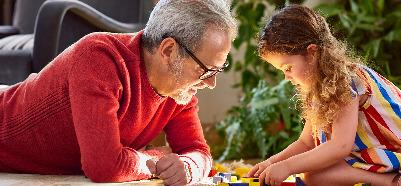 A foto mostra um idoso e uma criança brincando, representando um avô com sua neta.